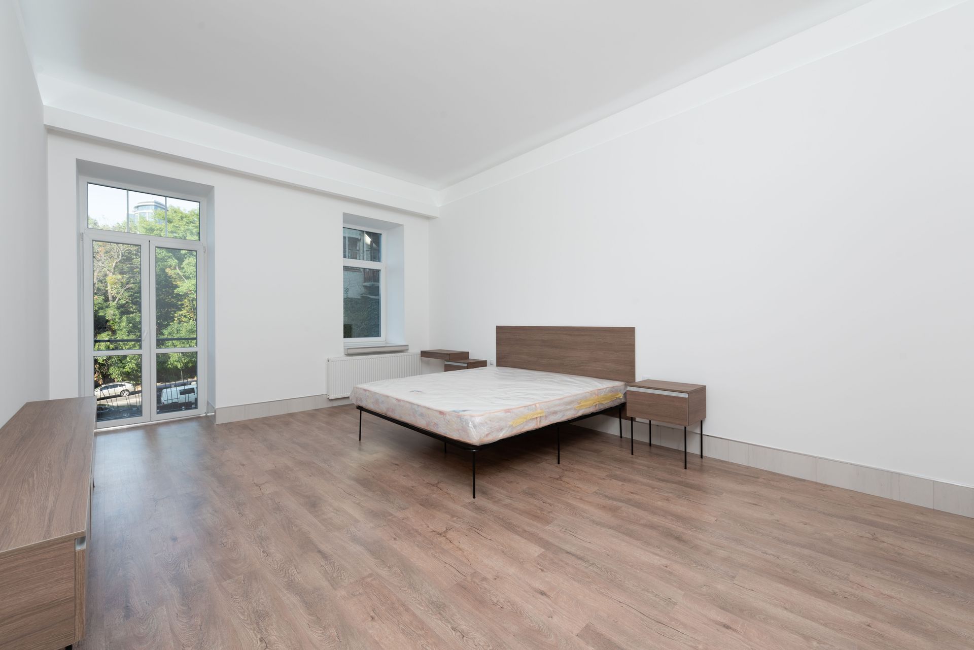 Spacious minimalist bedroom featuring wooden floors and large windows for natural light.